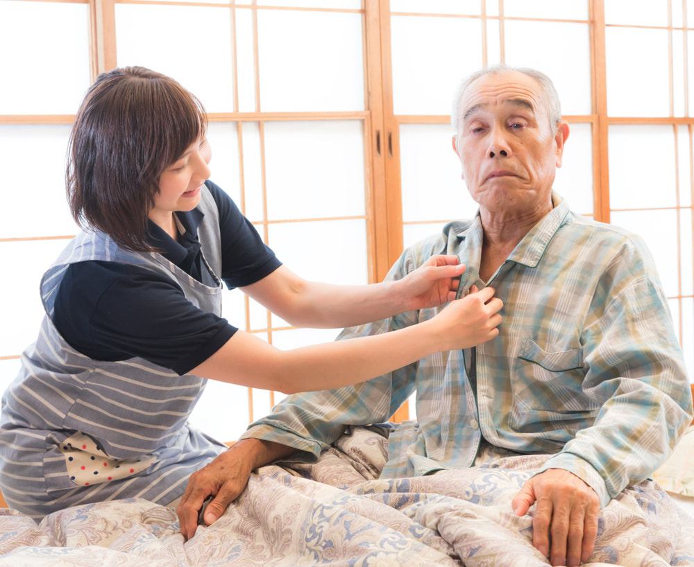 介護職員が高齢男性の健康状態を確認している場面。居室内での個別ケア。