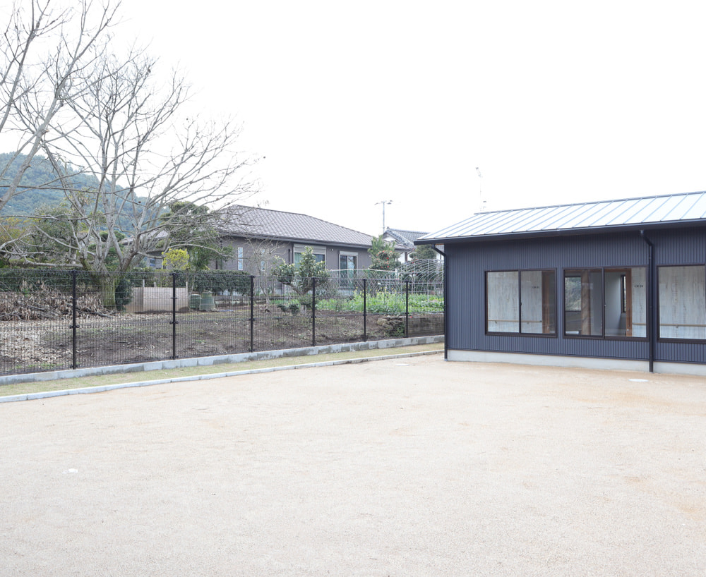施設の外構。砂利敷きの庭園エリアと黒色モダン建屋、フェンスで囲まれた安全な屋外スペース。